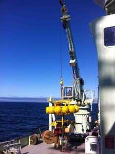 A crane lifts the tripod across the deck of the ship. 