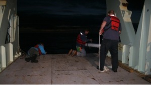 Figure 3. Very early morning (0200UTC) deployment of a RAFOS float over the eastern flank of the Reykjanes Ridge, July 2014 R/V Knorr. Float work is like CTD work, it happens anytime day or night. Here, the glass float is in the PVC deployment tube, which shelters the glass surface of the float from the rough deck. Although the glass survives well under extreme pressures of the deep ocean, scratches in the glass result in weak spots which can cause implosion. The first ten eastern flank Reykjanes Ridge floats are in the water, we have twenty more to go. (With Robb Hagg, Paul St. Onge, and Heather Furey.)