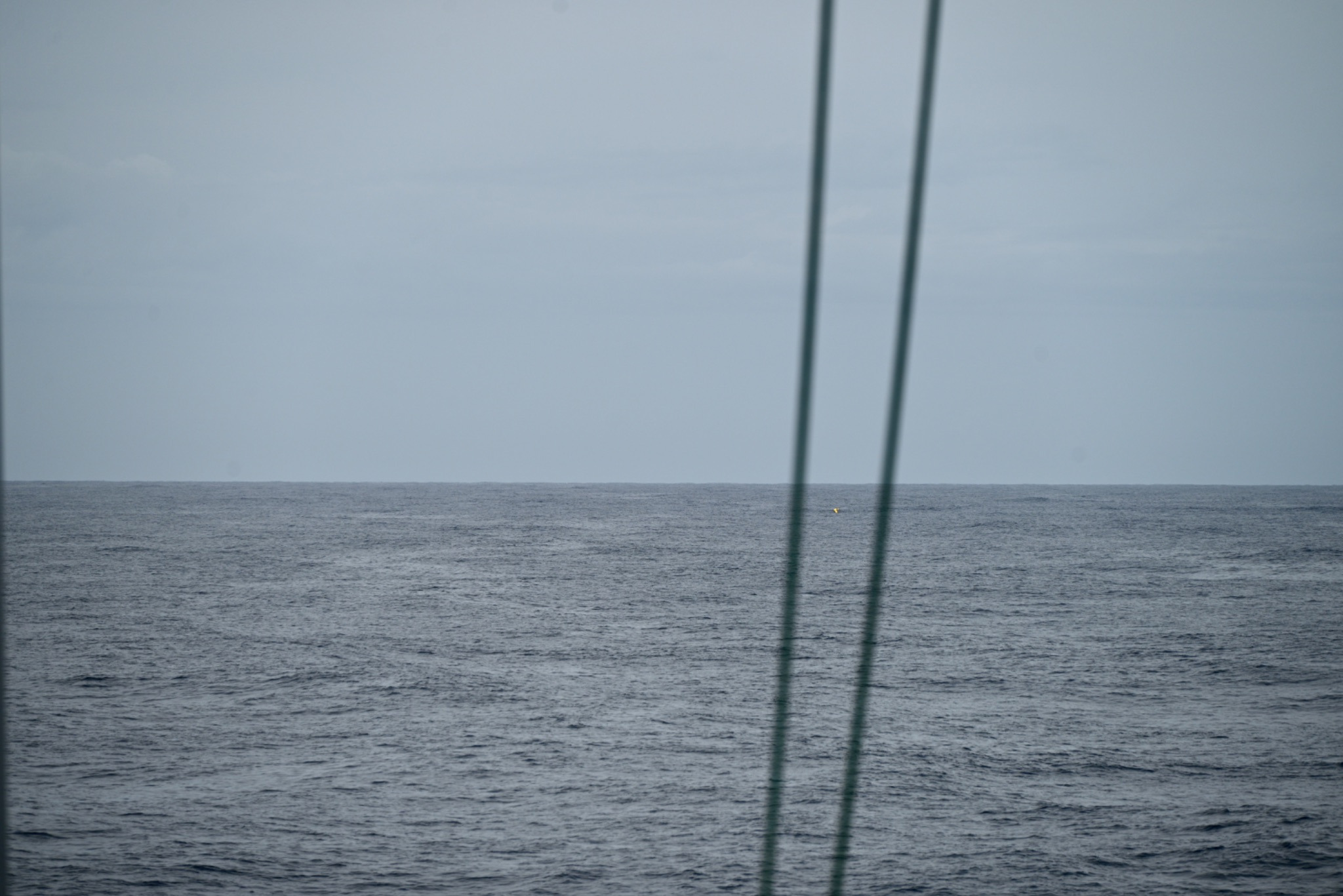 Photo of the deep, dark blue ocean with gray skies and a small yellow speck in the ocean.