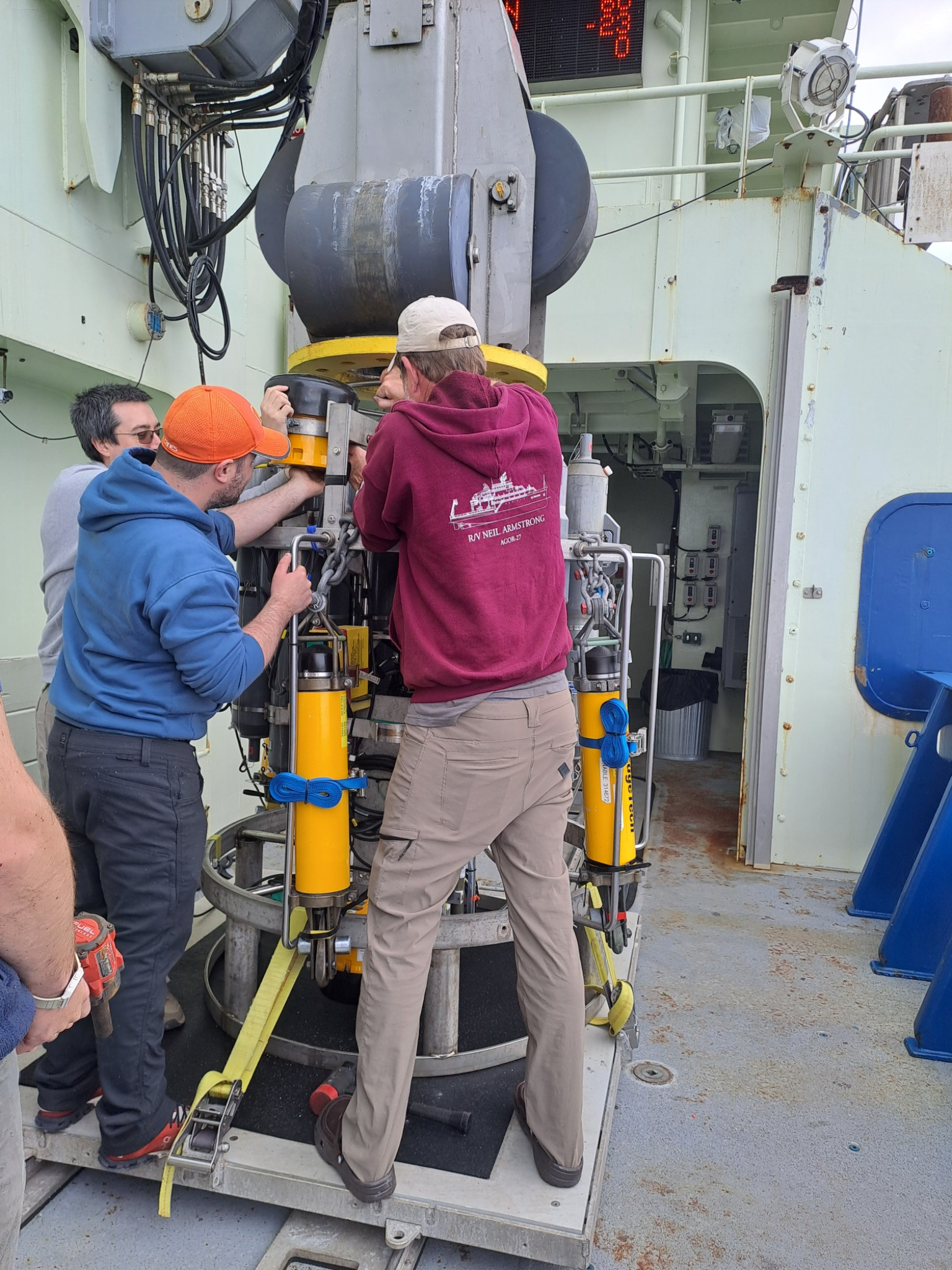Three people gather around the CTD rosette on the deck of a ship.